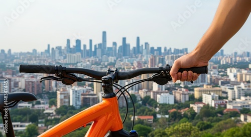 Hand gripping bicycle handlebars, with an orange bike in the foreground, overlooking a vibrant city skyline, showcasing urban cycling and outdoor adventure