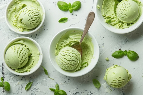 green ice cream scoops in white bowls with green leaves scattered around on a light textured background. A perfect summer treat background