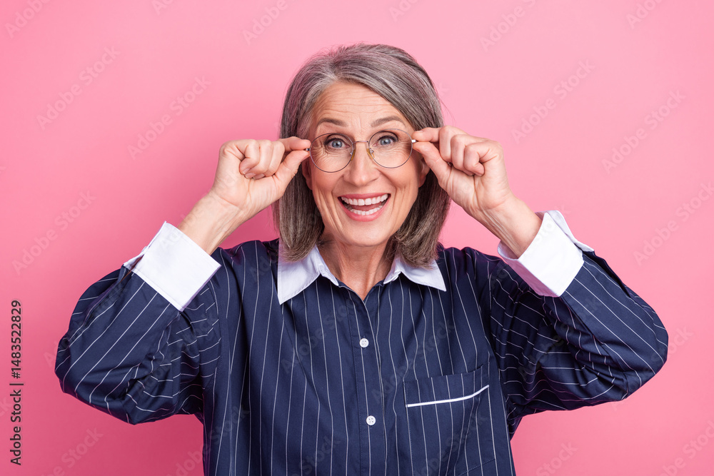 Cheerful senior woman with glasses smiling confidently, stylish in striped blouse on pink background, posing happily Cheerful senior woman with glasses smiling confidently, stylish in striped blouse on pink background, posing happily