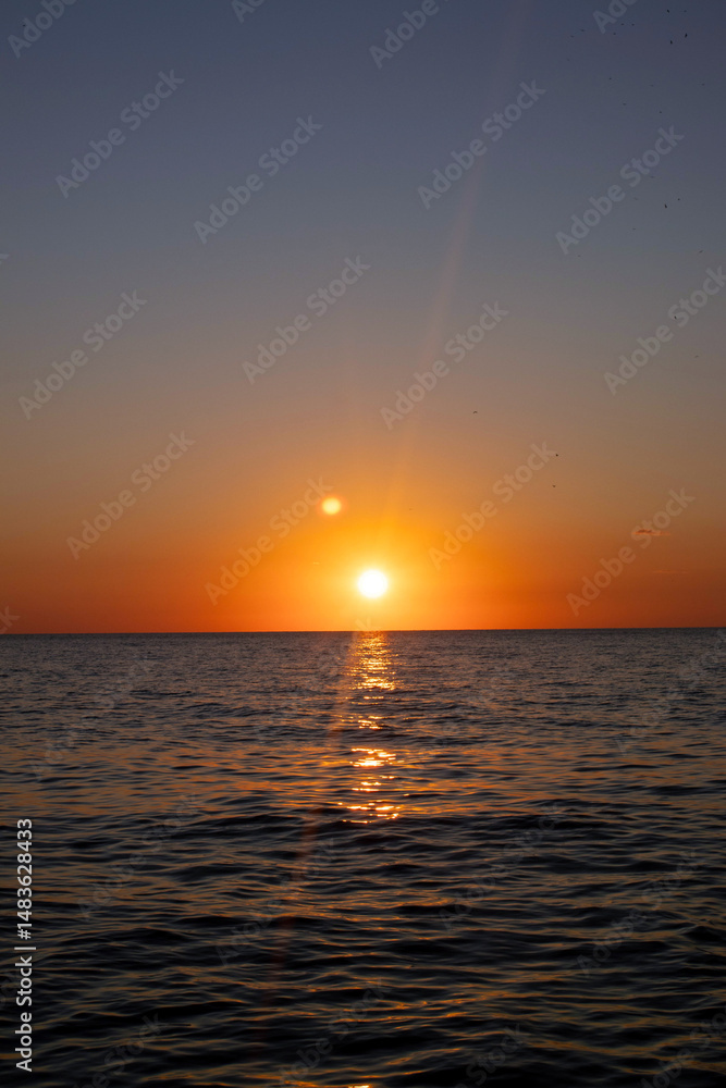 Fototapeta premium The sun is setting over the ocean, casting a warm glow on the water