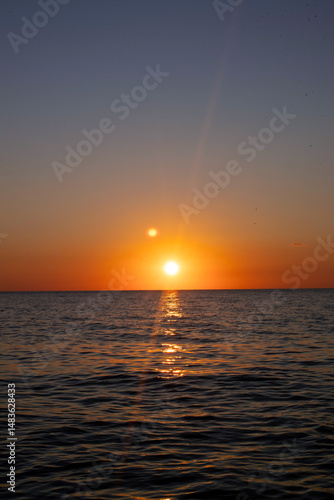 The sun is setting over the ocean, casting a warm glow on the water