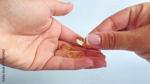 Female hand takes pills and vitamins on light background. Girl holds pills in hands. Vitamin omega 3, close-up. Home treatment, vitamins and supplements.
