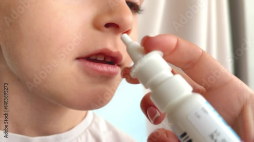 Mother uses nasal aspirator, snot sucker and nasal spray to spray saline solution into her baby's nose, little boy has runny nose and cold