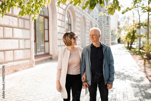 Senior happy couple of stylish man and woman 60-65 year old walking together on streets at city outdoors. Wellness lifestyle.