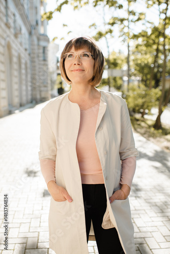 Smiling blonde senior woman 55-60 year old wearing eye glasses travelling in european city close up. Wellness mature lifestyle.