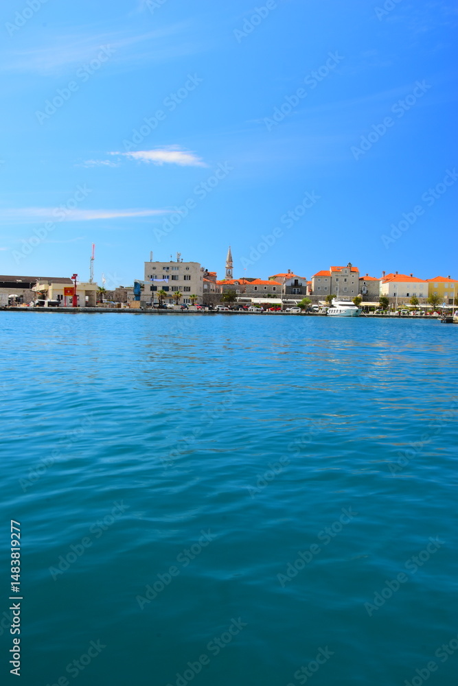 Obraz premium Budva, Montenegro - May 04, 2024: Dukley Marina and Old Town. The old city walls of Budva along the Adriatic coast, Montenegro. On a hot, sunny, spring afternoon.