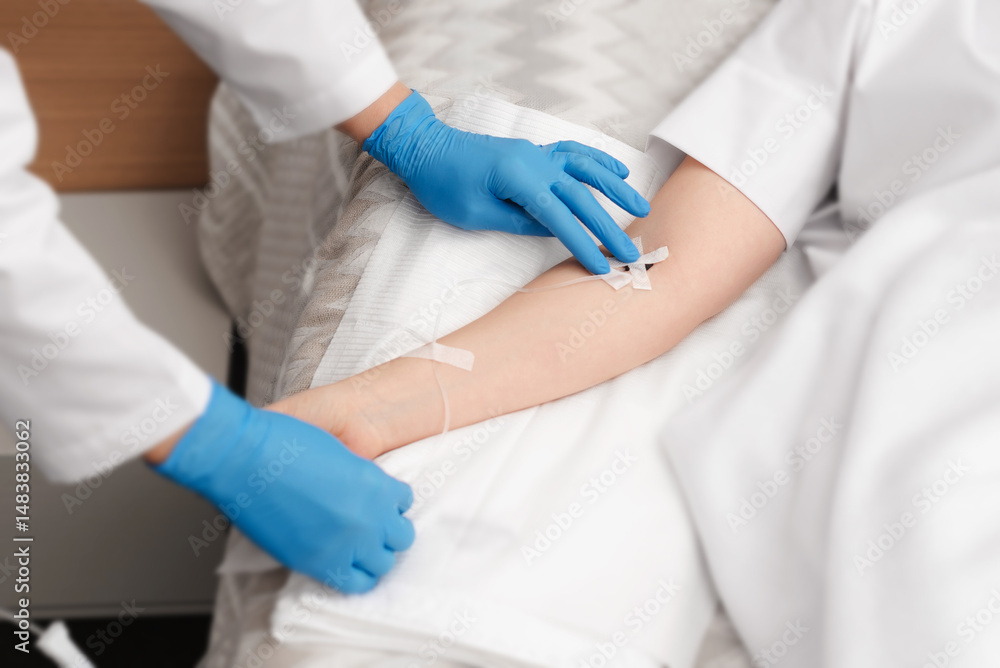 Doctor putting a drip to a patient for intravenous therapy. Woman hands in sterile gloves install a catheter for intravenous administration of drugs to a patient Doctor putting a drip to a patient for intravenous therapy. Woman hands in sterile gloves install a catheter for intravenous administration of drugs to a patient