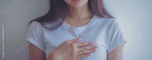 A woman in a white t shirt with her hand on her chest in a simple studio setting with soft lighting