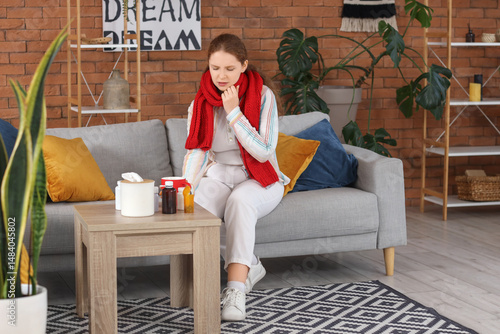 Sick young woman with cup of tea and medicine at home