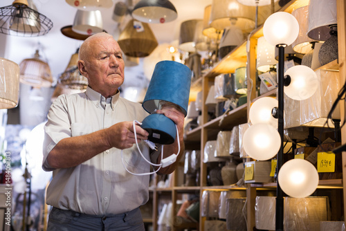 Portrait of mature man customer choosing table lamp at store of household goods