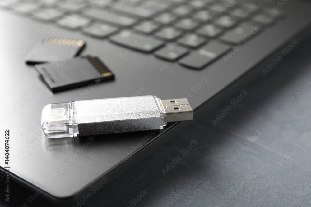 Fototapeta premium Usb flash drive, SD memory cards and laptop on grey textured table, closeup