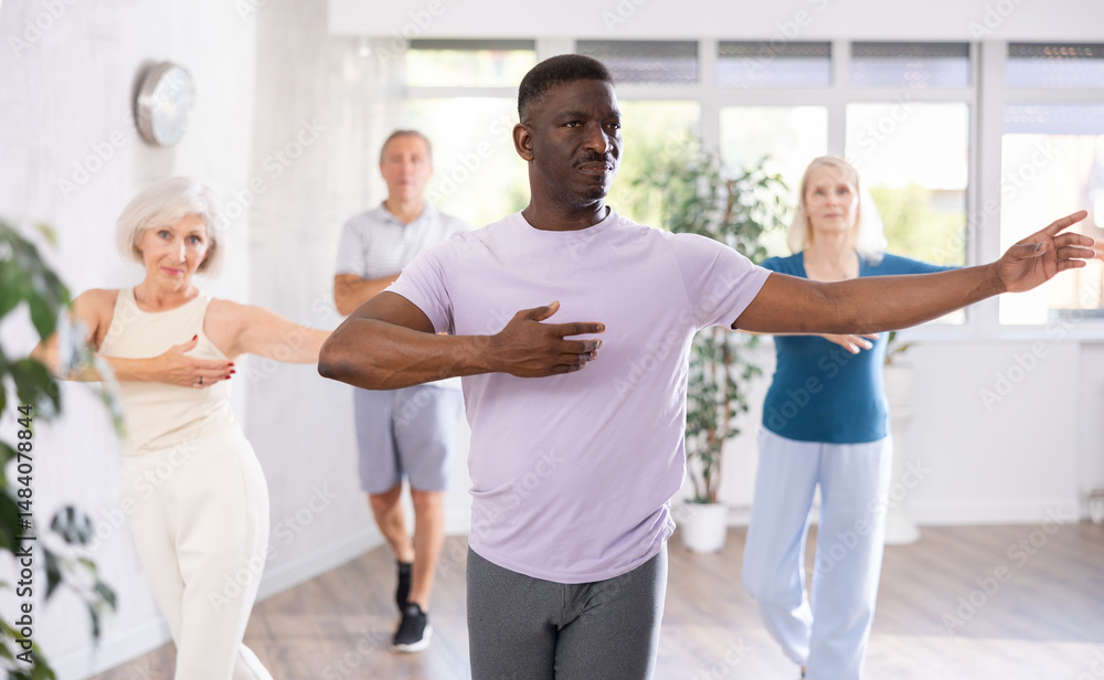 Obraz premium Positive interested adult african american man practicing slow partner dance movements during group class in modern choreography studio