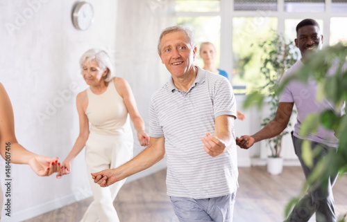 Senior europian man is engaged in modern dance class with group friends of different age and learn to perform movements to rhythmic music. Physical activity, good bodily shape