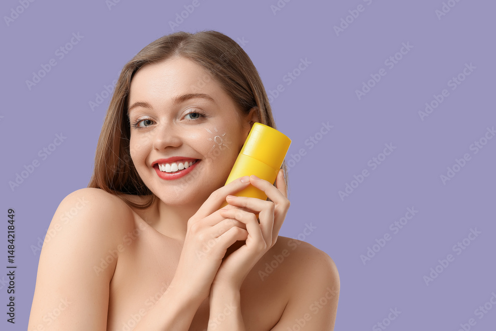 Beautiful young woman with sun made from sunscreen cream on her face and bottle against lilac background