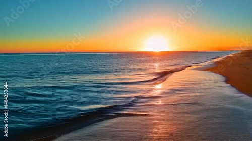 Ocean waves gently washing over the warm sandy beach with a stunning sunset sky and bright orange sun