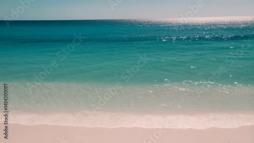 Tranquil beach scene with clear turquoise water and light colored sand under a sunny sky.