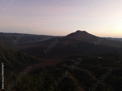 Stunning drone shot of Lake Batur at dawn, with mountain silhouettes reflecting on calm water under a colorful sky