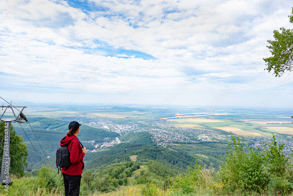 Naklejka premium Woman hiker standing on mountain trail, looking at forested hills.