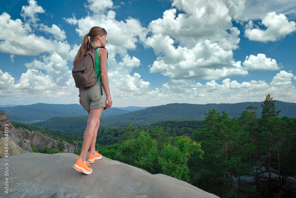 Naklejka premium Young woman hiking alone on mountain footpath. Female hiker enjoying view of summer nature on wilderness trail. Active way of life concept