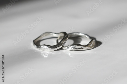 Two unique handmade silver rings free form elegantly displayed on smooth white surface. 