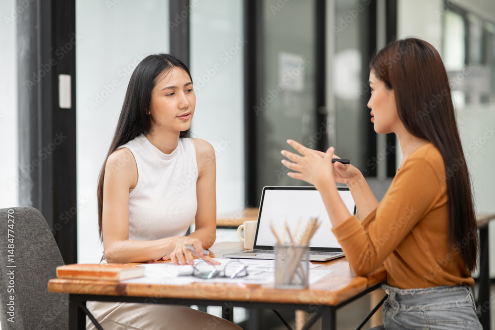 Two Asian businesswomen holding paper documents sit and talk happily. Two Asian businesswomen holding paper documents sit and talk happily.