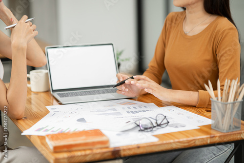 Two Asian businesswomen holding paper documents sit and talk happily.