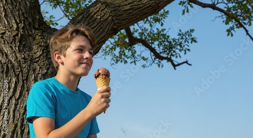 Young boy enjoying ice cream cone while sitting under tree  