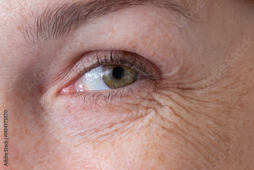 Cropped eye with wrinkles of middle aged caucasian woman smiling and looking at camera