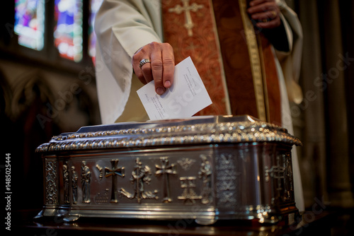 Priest putting donation in a silver box at a church ceremony symbolizing charity or giving.