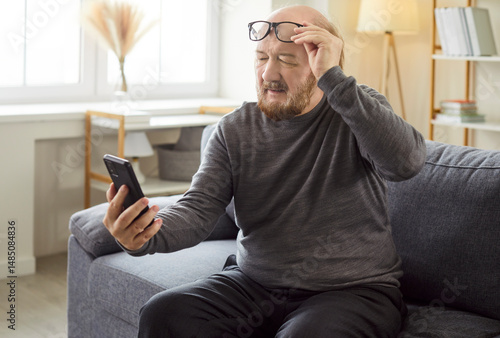 Worried confused senior man at home holding cellphone, unable watching phone screen, internet connection problem, frustrated aged grandfather feels sad, disappointed having new smartphone app