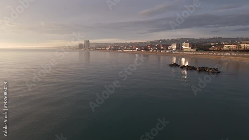 Aerial drone video of the Adriatic Sea at sunrise off Porto Potenza, Italy. Peaceful flyby capturing calm waters, golden reflections, and serene coastal beauty.