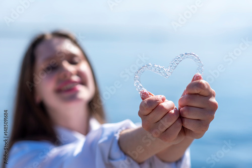 Dental care. Smiling beautiful woman holding heart-shaped aligners. Plastic retainers for teeth alignment.