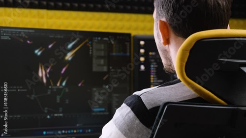 A male digital artist is designing vivid motion graphics on professional software at a dual-monitor workstation. The setting is a modern, acoustically treated creative studio.