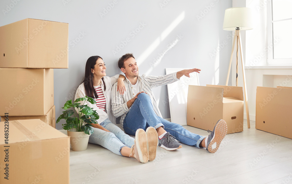 Portrait of a young happy couple man and woman sitting on floor in empty new apartment among cardboard boxes planning repair or design interior. Relocating, real estate, mortgage concept. Portrait of a young happy couple man and woman sitting on floor in empty new apartment among cardboard boxes planning repair or design interior. Relocating, real estate, mortgage concept.