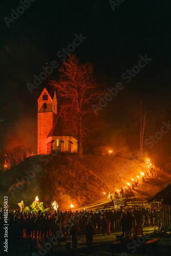 Night scene of a crowd watching a torchlit procession leading to a church on a hill. Krampus and St Nicholas, 5 December in Camporosso Valcanale, Tarvisio, Italy.