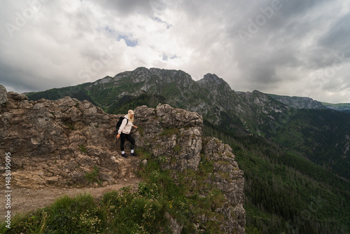 Female tourist enjoys a breathtaking view of Mount Giewont in Zakopane, Polish Tatra Mountains, on a cloudy day.