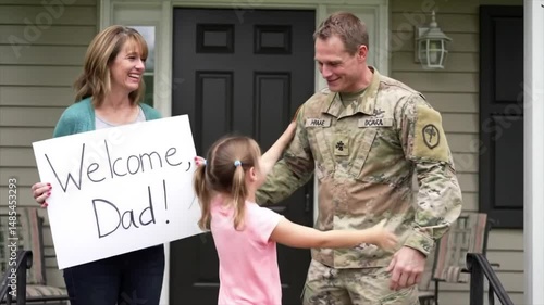A soldier surprises his family by arriving home after deployment. His wife holds a sign that says Welcome Dad! as their daughter runs to greet him