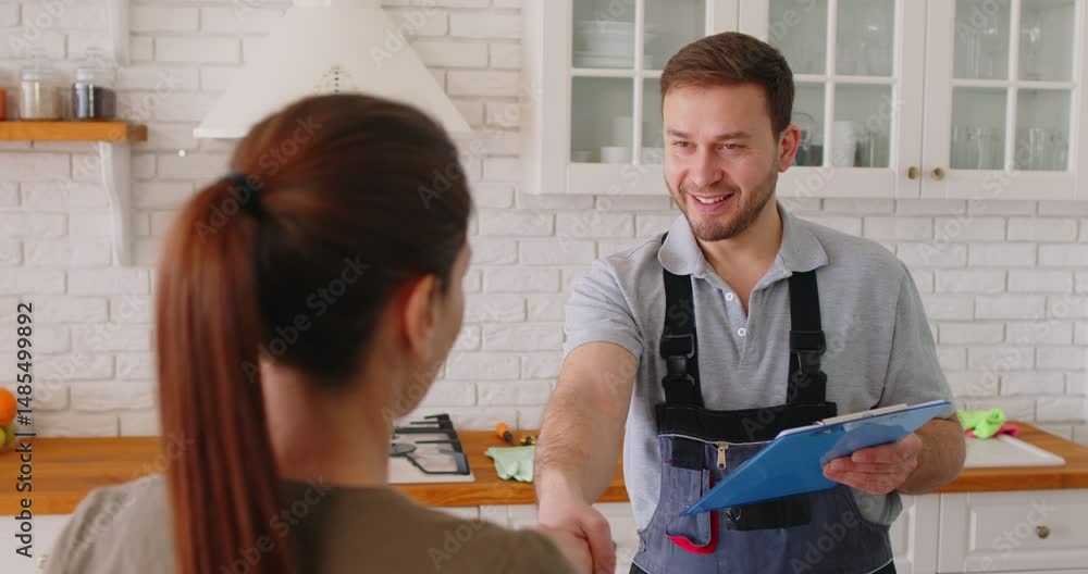Man maintenance worker or plumber shaking hands with woman client, satisfied after good quality service, standing in kitchen. Professional repairman in uniform has successful deal with client