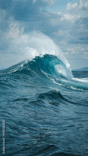 Powerful turquoise ocean wave crashes dramatically under a cloudy sky