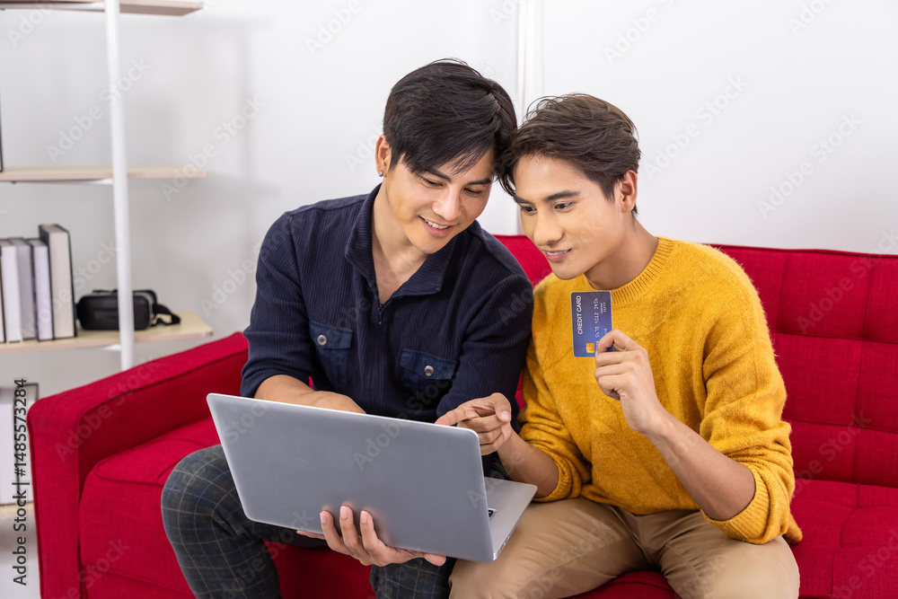 Fototapeta premium Asian LGBT gay couple shopping online with laptop and credit card at home on red sofa