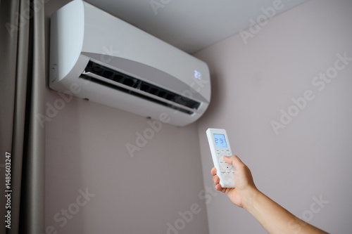Man holds remote control in front of an air conditioner, adjusting its temperature. Man sets air conditioner to comfortable temperature of 22 degrees Celsius