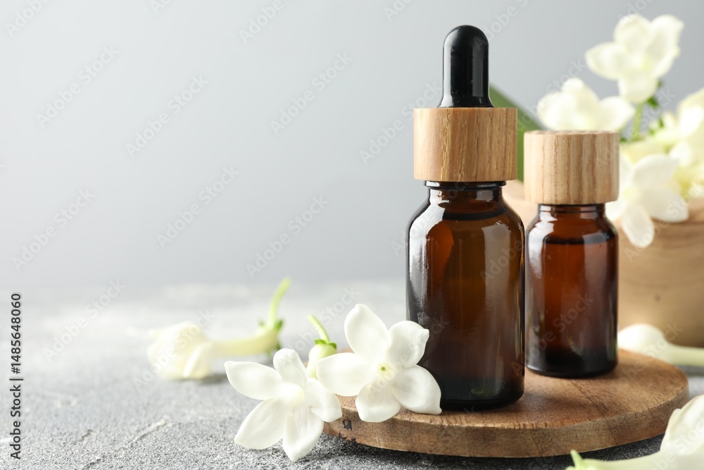 Bottles of essential oil and jasmine flowers on grey table, closeup. Space for text Bottles of essential oil and jasmine flowers on grey table, closeup. Space for text
