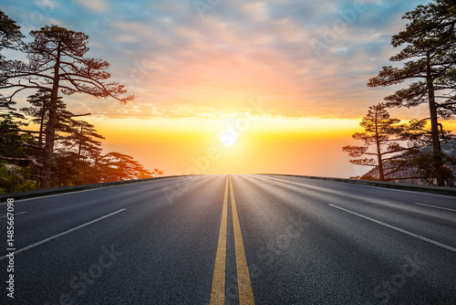 Empty asphalt road and pine trees with beautiful sky clouds at sunset