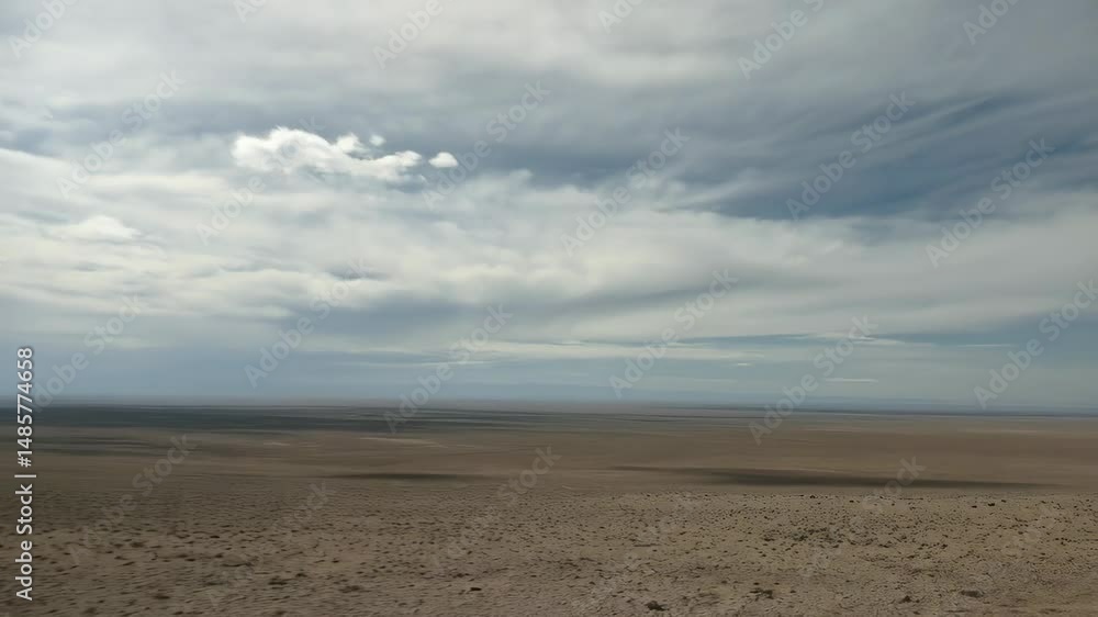 Solemn woman with dark hair gazes over a vast arid landscape, under a cloudy sky, wearing a dark textured tunic, looking forward with stoic expression. Solemn woman with dark hair gazes over a vast arid landscape, under a cloudy sky, wearing a dark textured tunic, looking forward with stoic expression.
