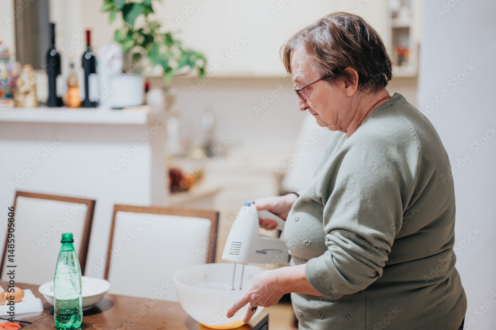 Elderly woman standing in a kitchen, attentively mixing ingredients in a bowl, emphasizing home cooking and culinary activities. Elderly woman standing in a kitchen, attentively mixing ingredients in a bowl, emphasizing home cooking and culinary activities.