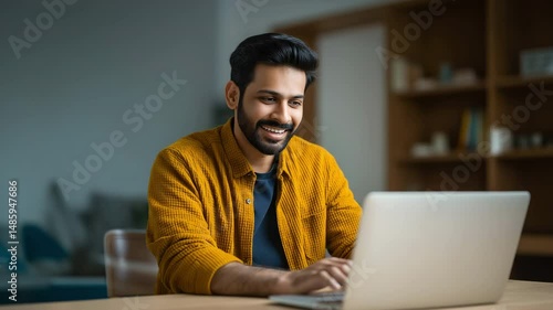 Indian businessman smiles while using a laptop in his home office. 