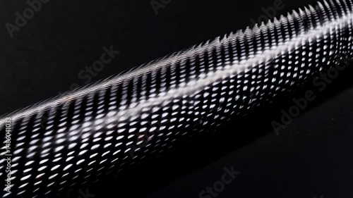 Close-up of a cylindrical object with a shiny, black and white checkered pattern against a dark background showing texture and surface details.