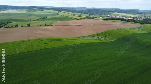 Aerial view of rolling agricultural fields and green pastures surrounding small village in scenic countryside valley landscape