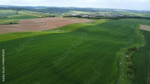 Aerial view of rolling agricultural fields and green pastures surrounding small village in scenic countryside valley landscape