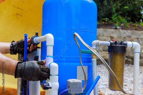 Plumber connects pipes to artesian water well filtration tank during an installation process in backyard.
